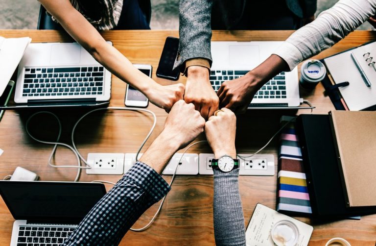 Five hands coming together over a desk